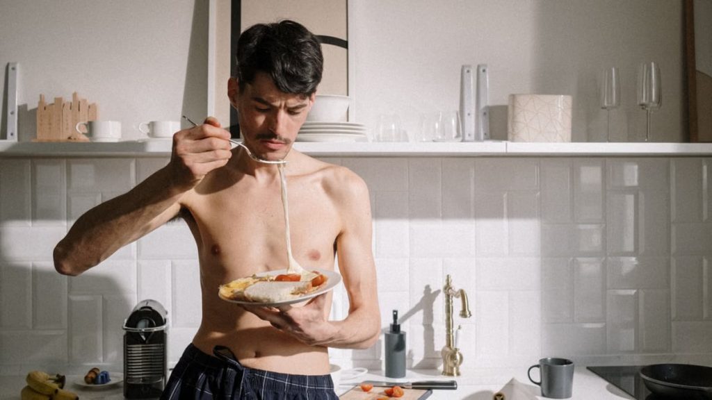 Young man enjoying a breakfast omelette in a sunlit kitchen setting.